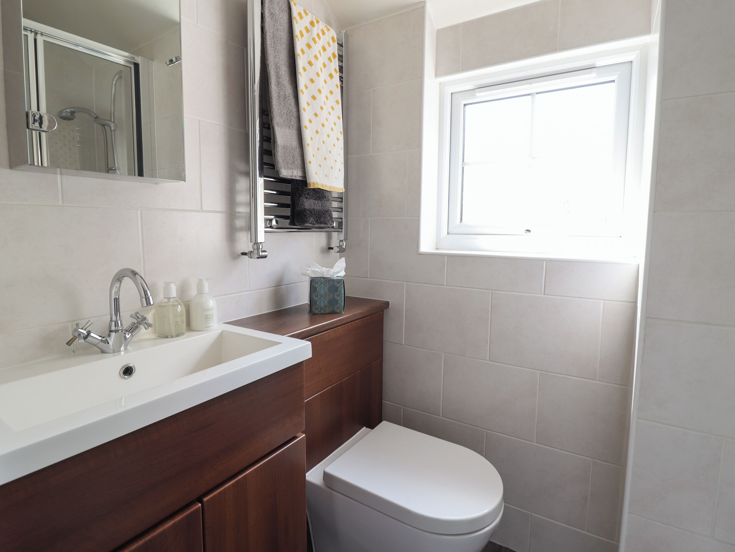 A bathroom with a white sink, a mirror, a towel rack with towels, a toilet, and a window.