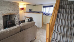 A cozy living room with a stone fireplace, a sofa, and a staircase with striped carpet. - Ty Bach Twt (Conwy)