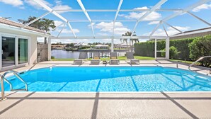 Une piscine dotée d’un espace couvert, de chaises longues et offrant une vue sur un lac et des maisons en arrière-plan.