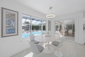 A modern dining area with a glass wall overlooking a pool, white furniture, and artwork on the walls. - Direct Boating Access | Olde Marco Home w/ Pool (Marco Island)