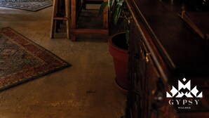 An interior with wooden beams, hanging wicker lamps, a dining area with stools, and potted plants. - Gipsy Village (Tetritskaro)