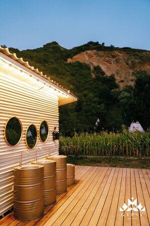 A rustic cabin with a wooden deck, three barrels, and a mountain backdrop. - Gipsy Village (Tetritskaro)