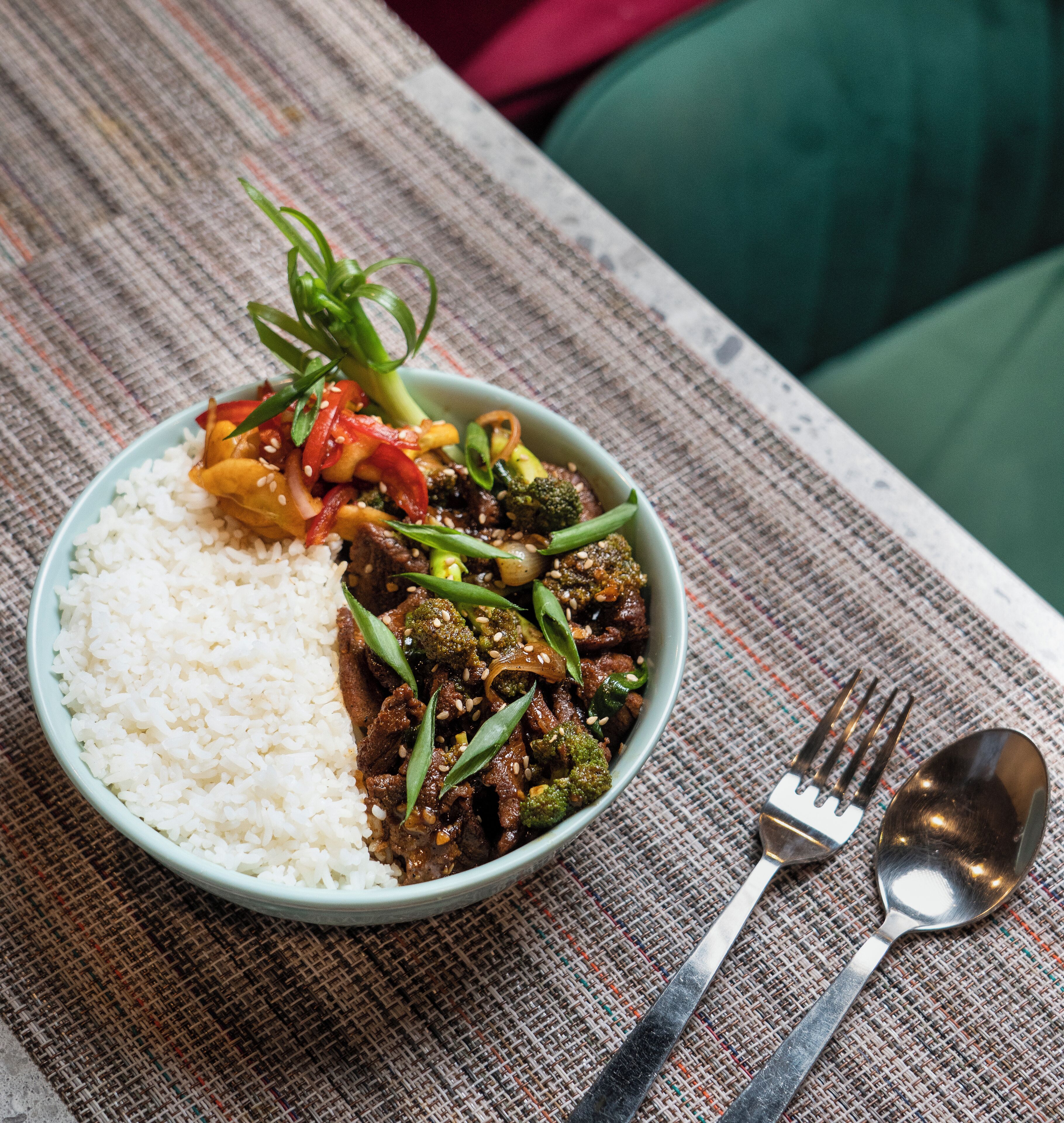Eine Schüssel mit Reis und gebratenem Gemüse mit Rindfleisch, serviert auf einer gewebten Unterlage.