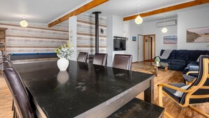 Een moderne woonkamer met een donker houten eettafel, lederen stoelen, een blauwe bank en een aan de muur bevestigde televisie.