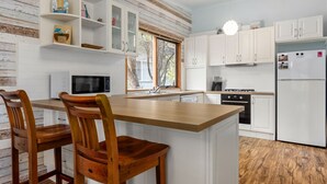 Een keuken met witte kastjes, een houten kookeiland met twee stoelen, een magnetron, een fornuis en een koelkast.