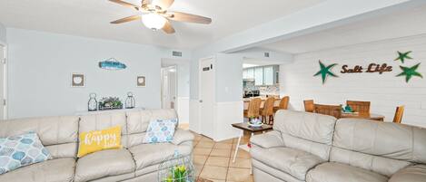 A living room with two beige sofas, a ceiling fan, and a dining area with wooden furniture.