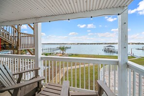 A wooden deck with a view of a lake, dock, and distant buildings. - Lagoon Run 102 | 3BR/2BA Lagoon-View Condo | Sleeps 6 | Coastal Escape (Gulf Shores)