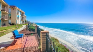 A beachfront hotel with a patio area featuring a blue chair, a brick pathway, and a view of the ocean. - 10% OFF last minute stays - Oceanfront 1 bedroom, Pool, Spa, Beach Access (Solana Beach)