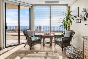 A room with wicker furniture, a view of the beach, and a sign reading 'LEUCADIA'. - 10% OFF last minute stays - Oceanfront 1 bedroom, Pool, Spa, Beach Access (Solana Beach)