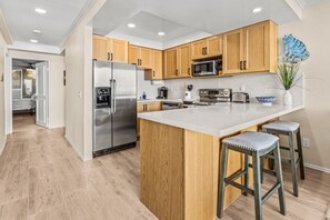 A modern kitchen with wooden cabinets, stainless steel appliances, and a central island with bar stools. - 10% OFF last minute stays - Oceanfront 1 bedroom, Pool, Spa, Beach Access (Solana Beach)