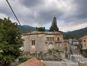 Un edificio histórico de piedra con una torre de campanas, una escalera y un paso de peatones en un pueblo montañoso.
