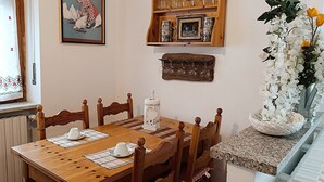 A dining area with a wooden table and chairs, a picture on the wall, and a shelf with glassware. - *merlin apartment near the Giaveno Sanctuary, 5 km from the Avigliana lakes (Giaveno)