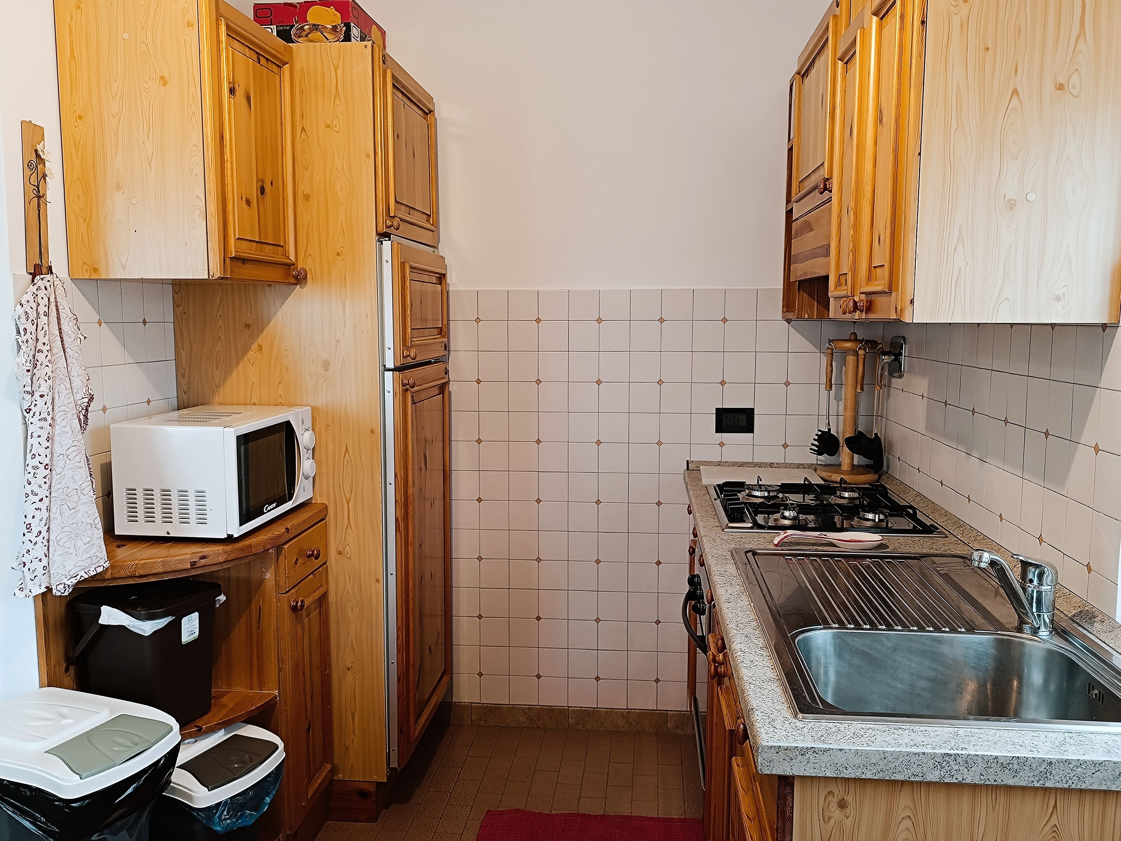 Una cocina compacta con armarios de madera, un microondas, una estufa a gas y un lavaplatos de acero inoxidable.