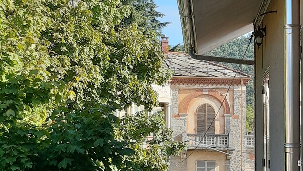 A balcony with a stone building in the background, a clear sky, and a tree in the foreground. - *merlin apartment near the Giaveno Sanctuary, 5 km from the Avigliana lakes (Giaveno)