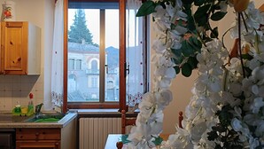 A kitchen with wooden cabinets, a window with curtains, a radiator, and a view of a building outside. - *merlin apartment near the Giaveno Sanctuary, 5 km from the Avigliana lakes (Giaveno)