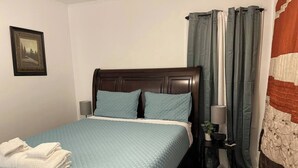 A neatly made bed with a blue quilt, a wooden headboard, and a nightstand with a lamp and a small plant. - Peaceful Retreat Near the Waterfront (Elizabeth City)
