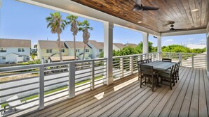 A covered outdoor deck with a wooden floor and white railings, overlooking a residential area with palm trees and houses.