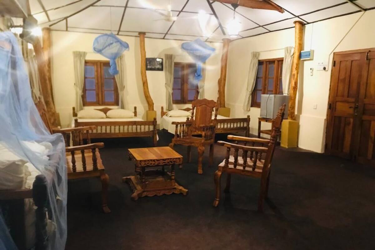 A room with a bed, two wooden chairs, a small table, and a television.