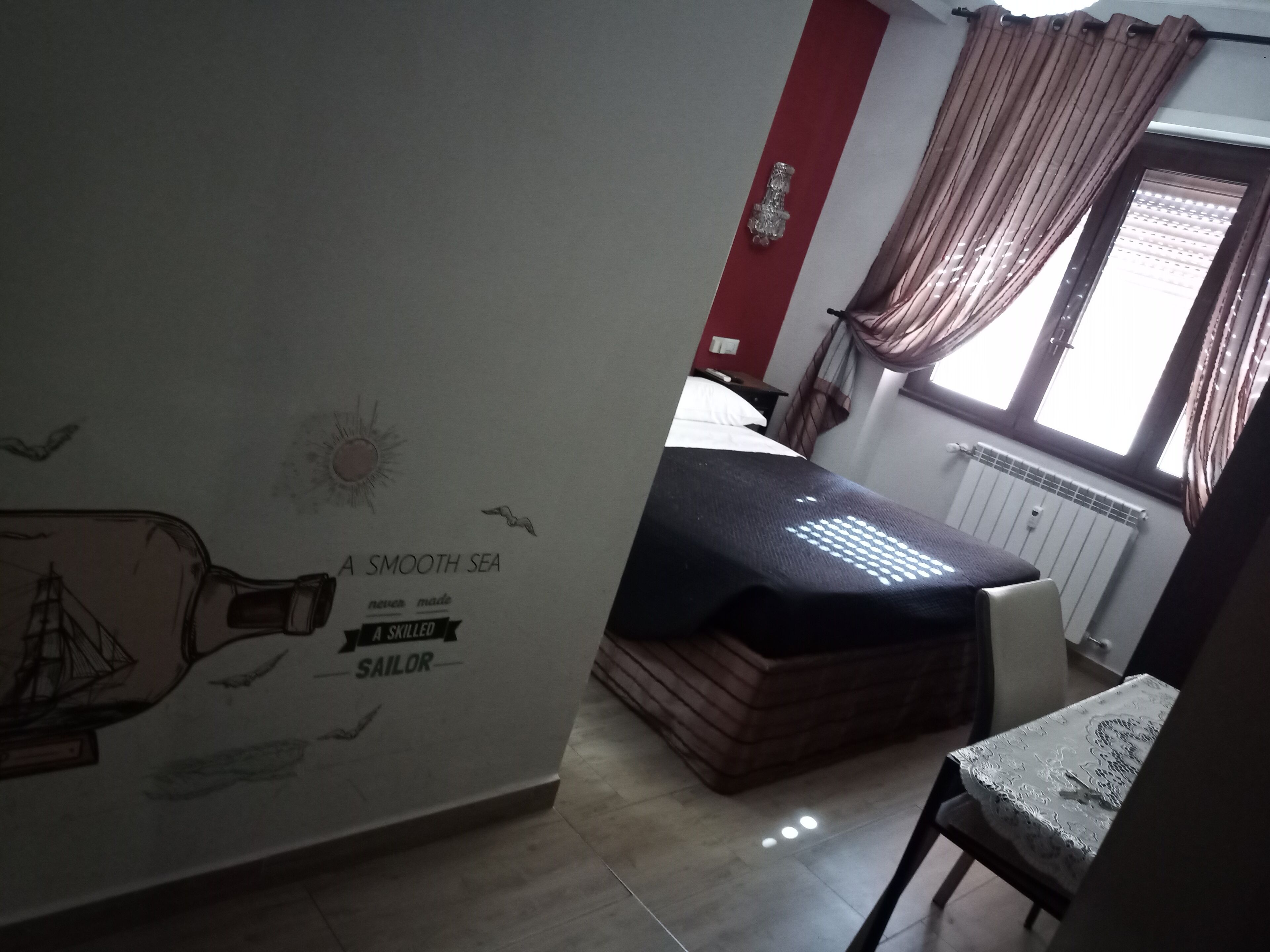 Un dormitorio con cama, mesita de noche, ventana con cortinas y decoración náutica en la pared.