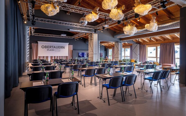 Un salón de conferencias con mesas y sillas, una pantalla grande y techo de madera.