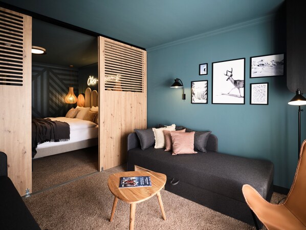 A modern bedroom with a bed, a sofa, a small wooden table, and a wall with framed pictures. - [PLACES] Obertauern by Valamar (Untertauern)