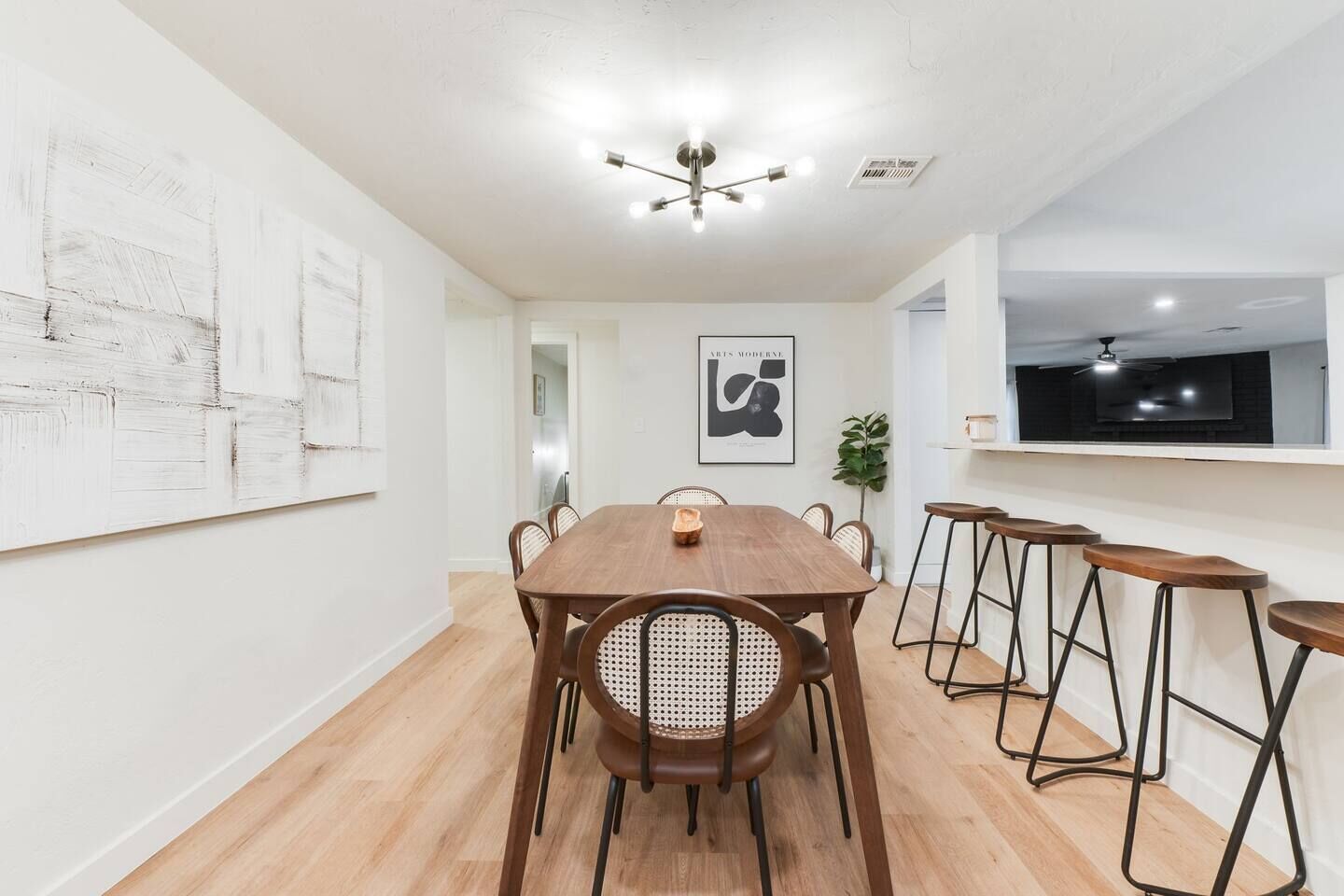 Un coin repas avec une table et des chaises en bois, un luminaire au plafond et un téléviseur fixé au mur.