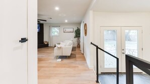 A spacious living area with a white sofa, a potted plant, and a staircase leading to an outdoor area. - Chateau Urbane- a luxe escape (Norman)