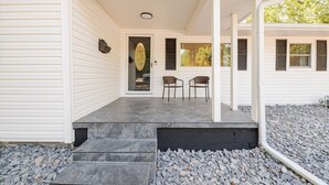 A covered porch with two chairs, a door with a decorative glass panel, and steps leading to the entrance. - Chateau Urbane- a luxe escape (Norman)