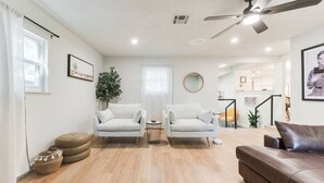 A spacious living area with two white armchairs, a brown sofa, a wooden floor, and a ceiling fan. - Chateau Urbane- a luxe escape (Norman)