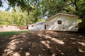 Une maison mobile de plain-pied avec un petit garage attenant, entourée d’une cour clôturée et d’arbres.
