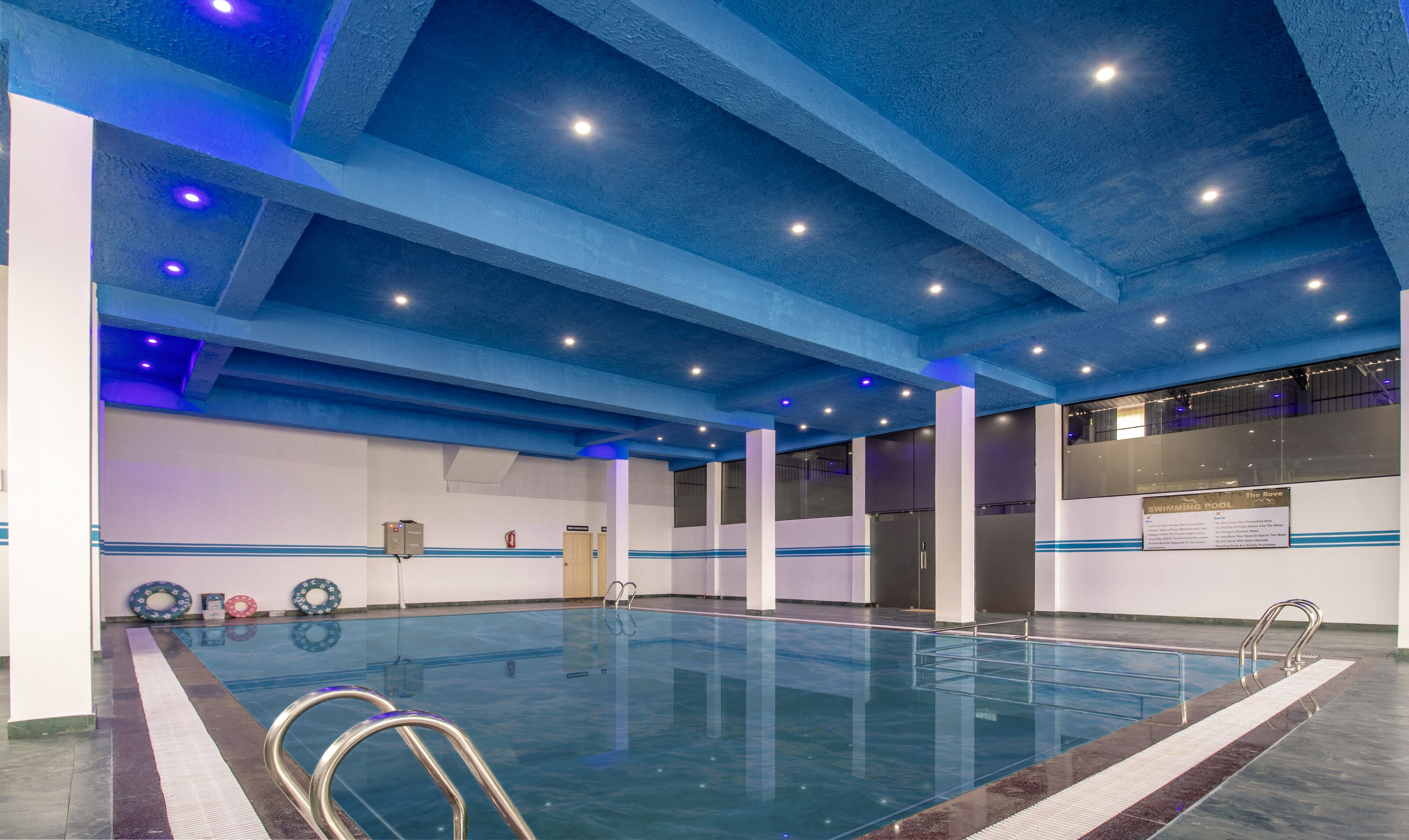 An indoor swimming pool with a blue ceiling, clear water, and a sign indicating 'Swimming Pool'.