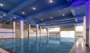 An indoor swimming pool with clear water, surrounded by walls with windows.