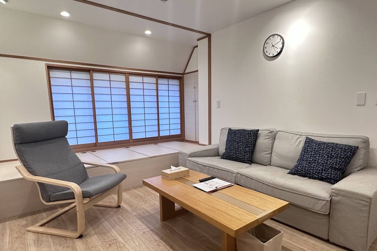 A modern living room with a sofa, a chair, a wooden coffee table, and a window with a view.