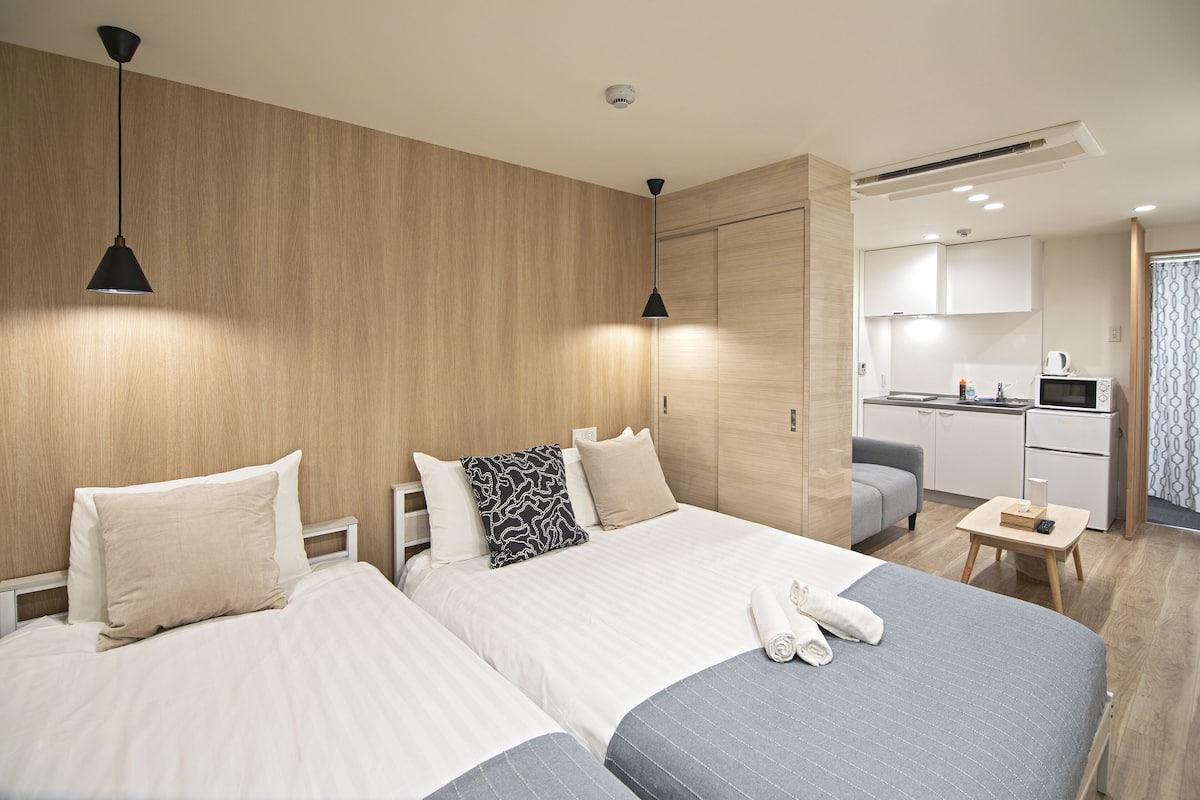 A hotel room with two beds, a kitchenette, and a small seating area.