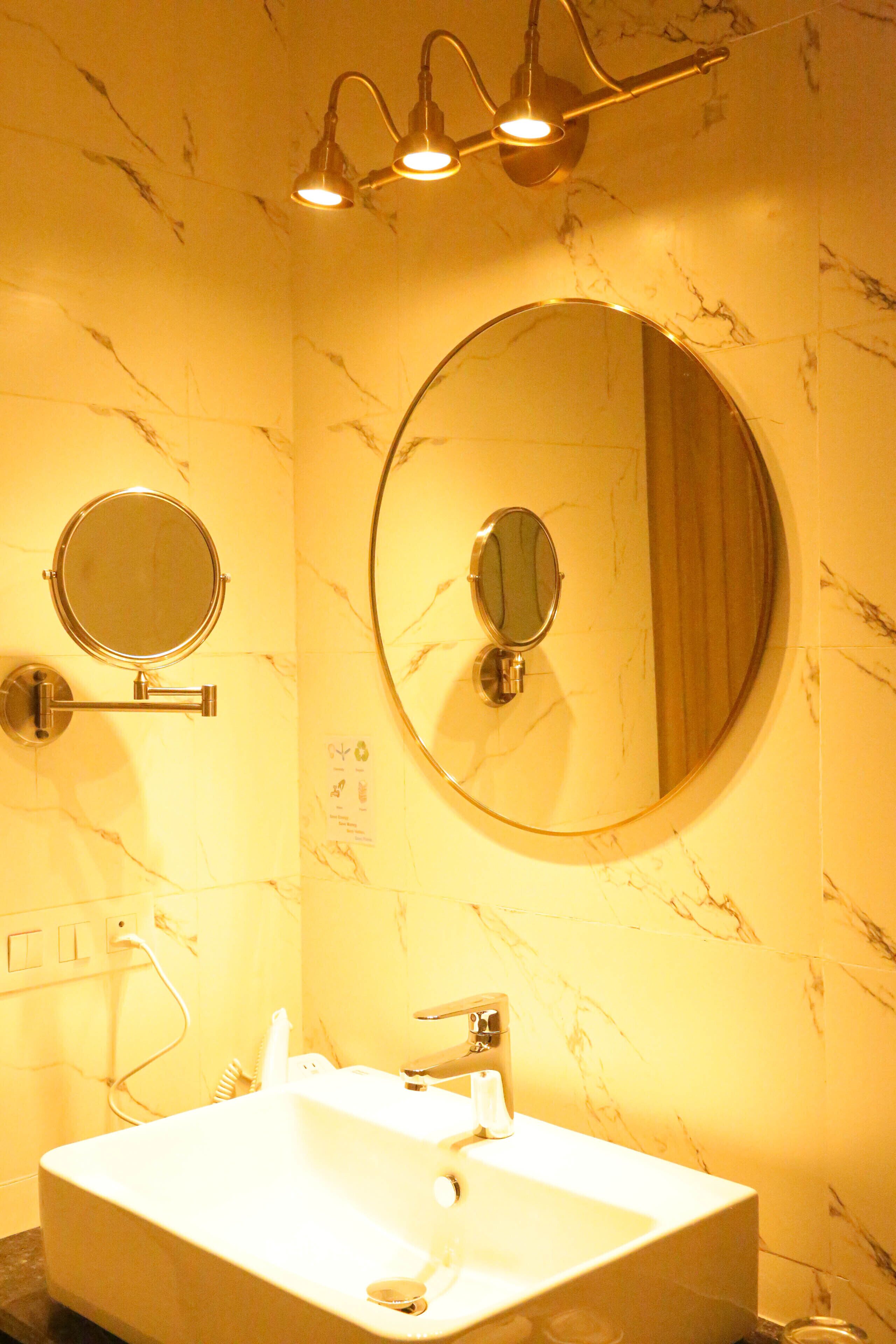 A bathroom with a large oval mirror, a round mirror, and a rectangular sink.