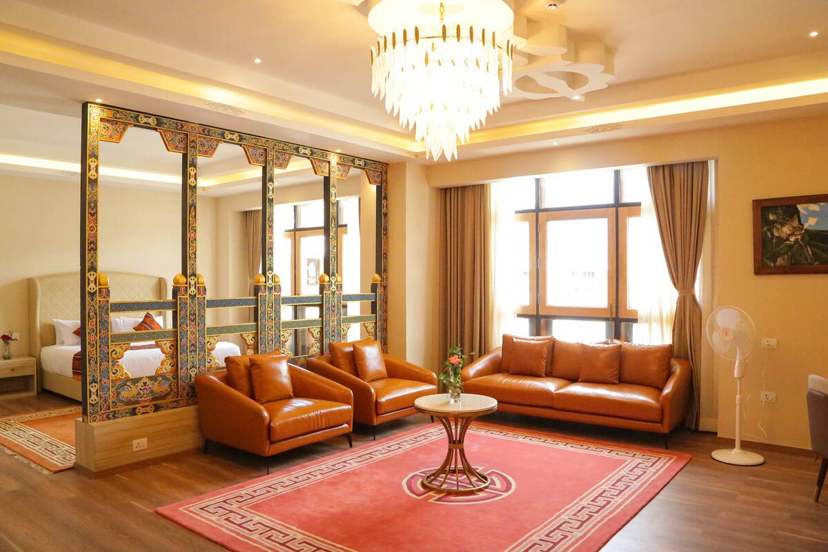 A spacious living room with a large ornate mirror, leather sofas, a round coffee table, and a chandelier.