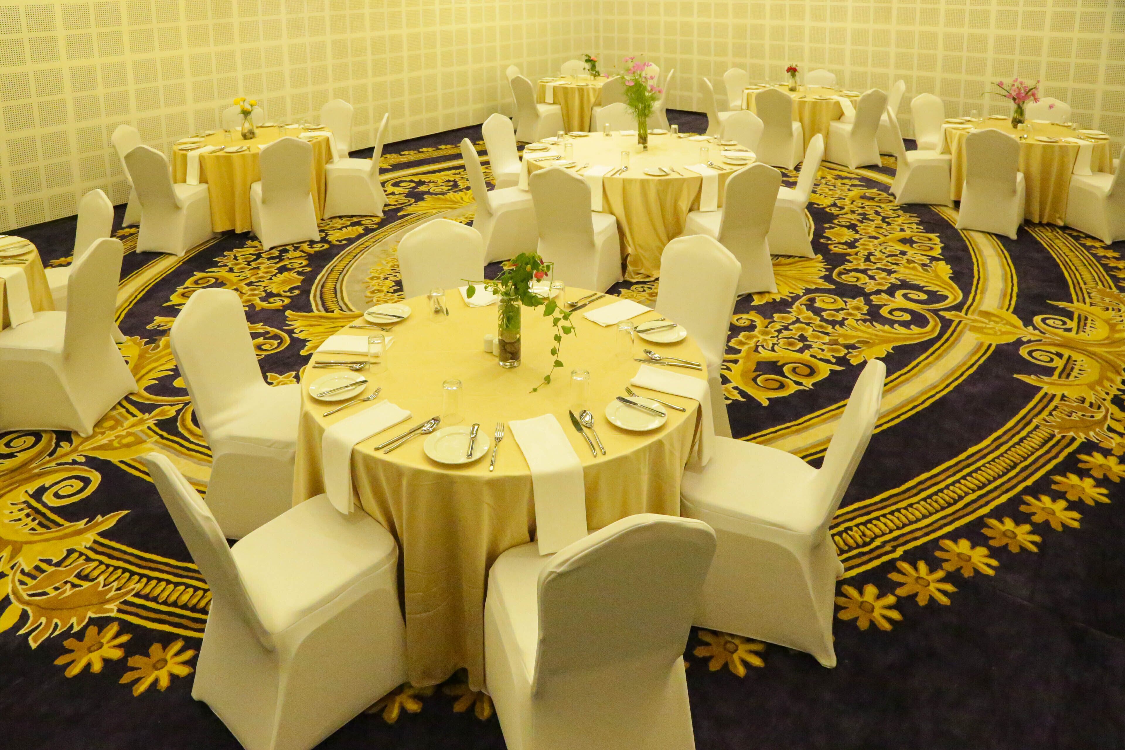 A conference room with round tables, white chairs, and a patterned carpet.