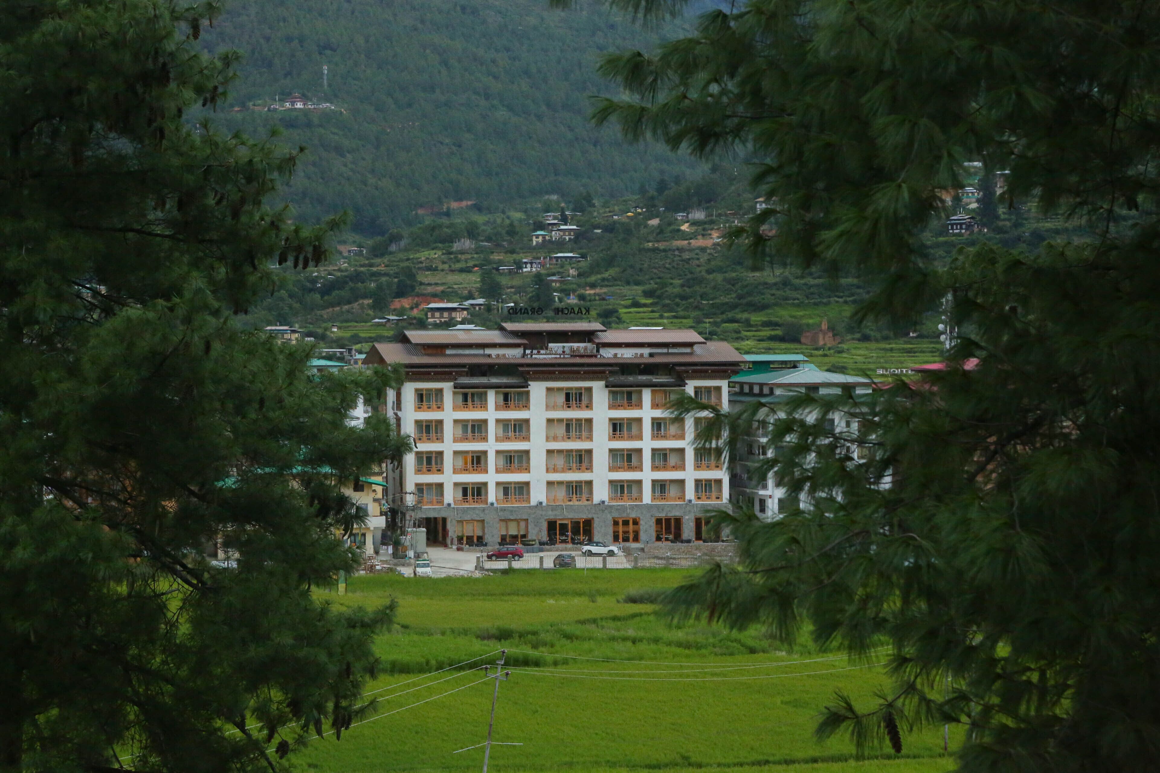 A multi-story hotel with a traditional architectural style, surrounded by lush greenery and a hilly landscape.