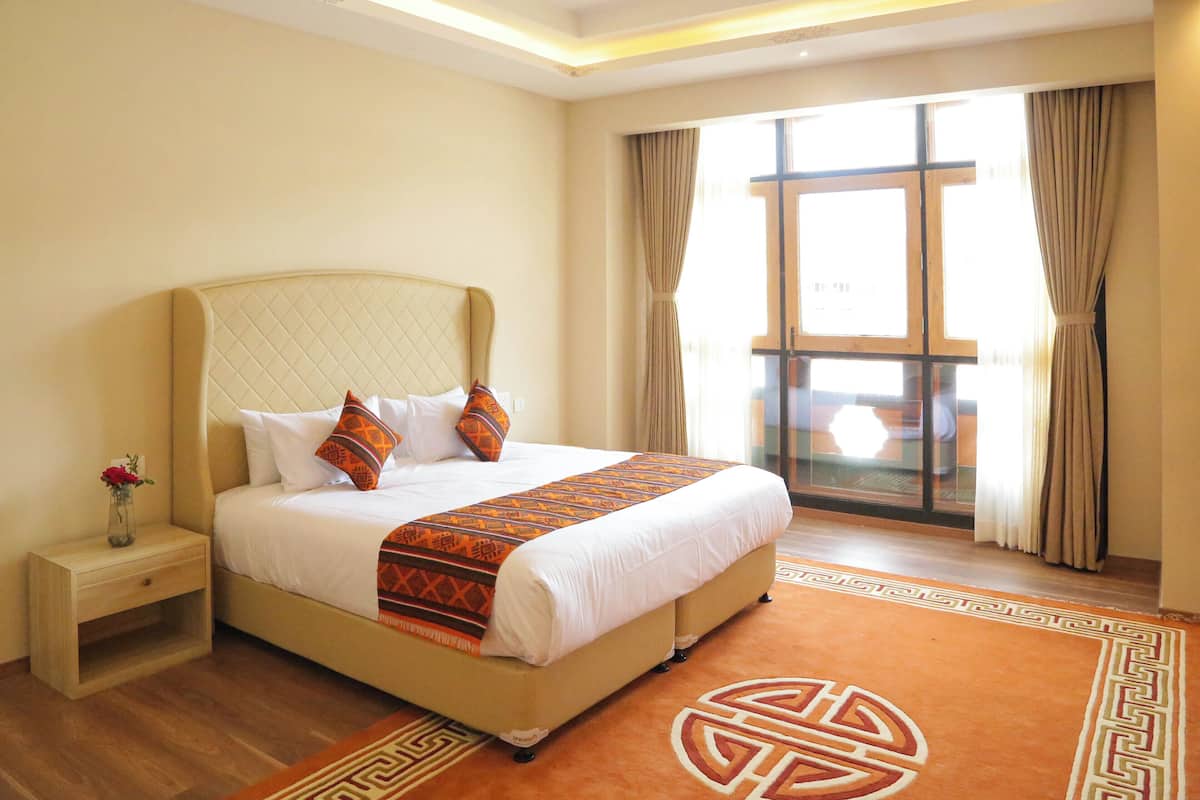 A hotel room with a large bed, a nightstand with a vase of flowers, and a view of the outside through a large window.
