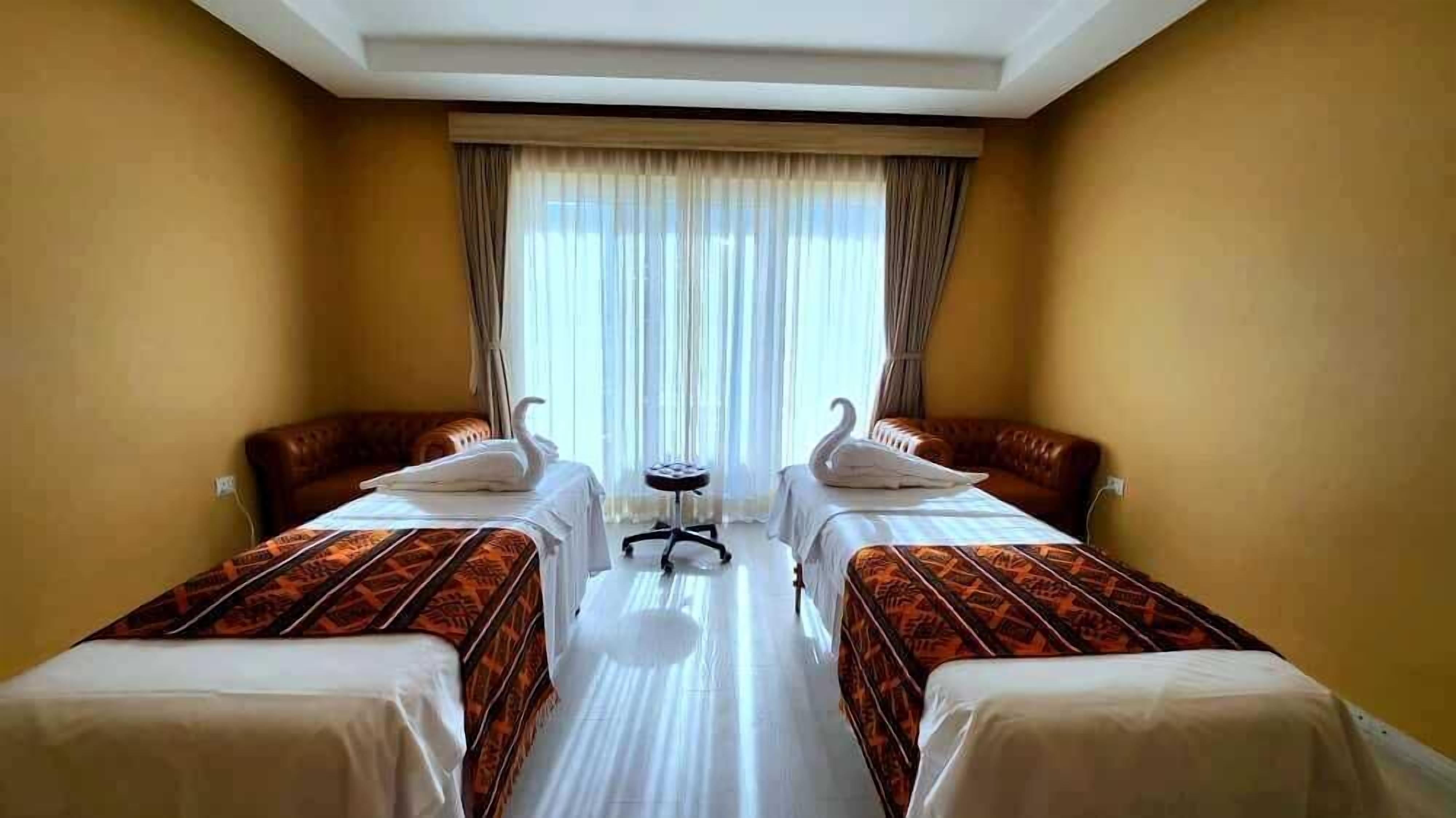 A hotel room with two beds, a small table, and a window with curtains.