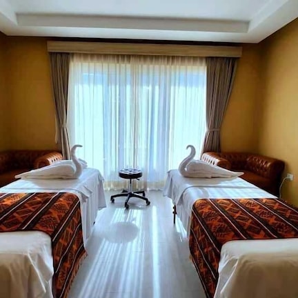 A hotel room with two beds, a small table, and a window with curtains.