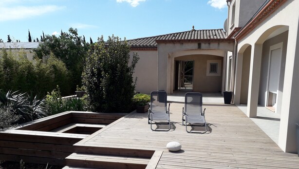 A patio with two lounge chairs, a wooden deck, and a stone feature. - House between sea, pool and garrigue (Cuxac-d'Aude)