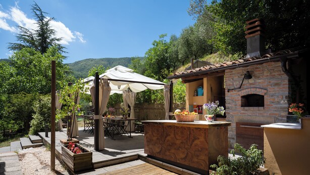 A patio with a wooden deck, outdoor seating, a brick oven, and a pergola with a white canopy. - Podere La Vigna (Borgo San Lorenzo)