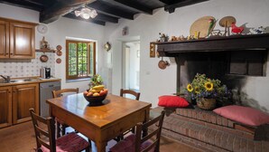 A kitchen with wooden cabinets, a dining table with chairs, a red cushion, a basket of flowers, and a brick fireplace. - Podere La Vigna (Borgo San Lorenzo)