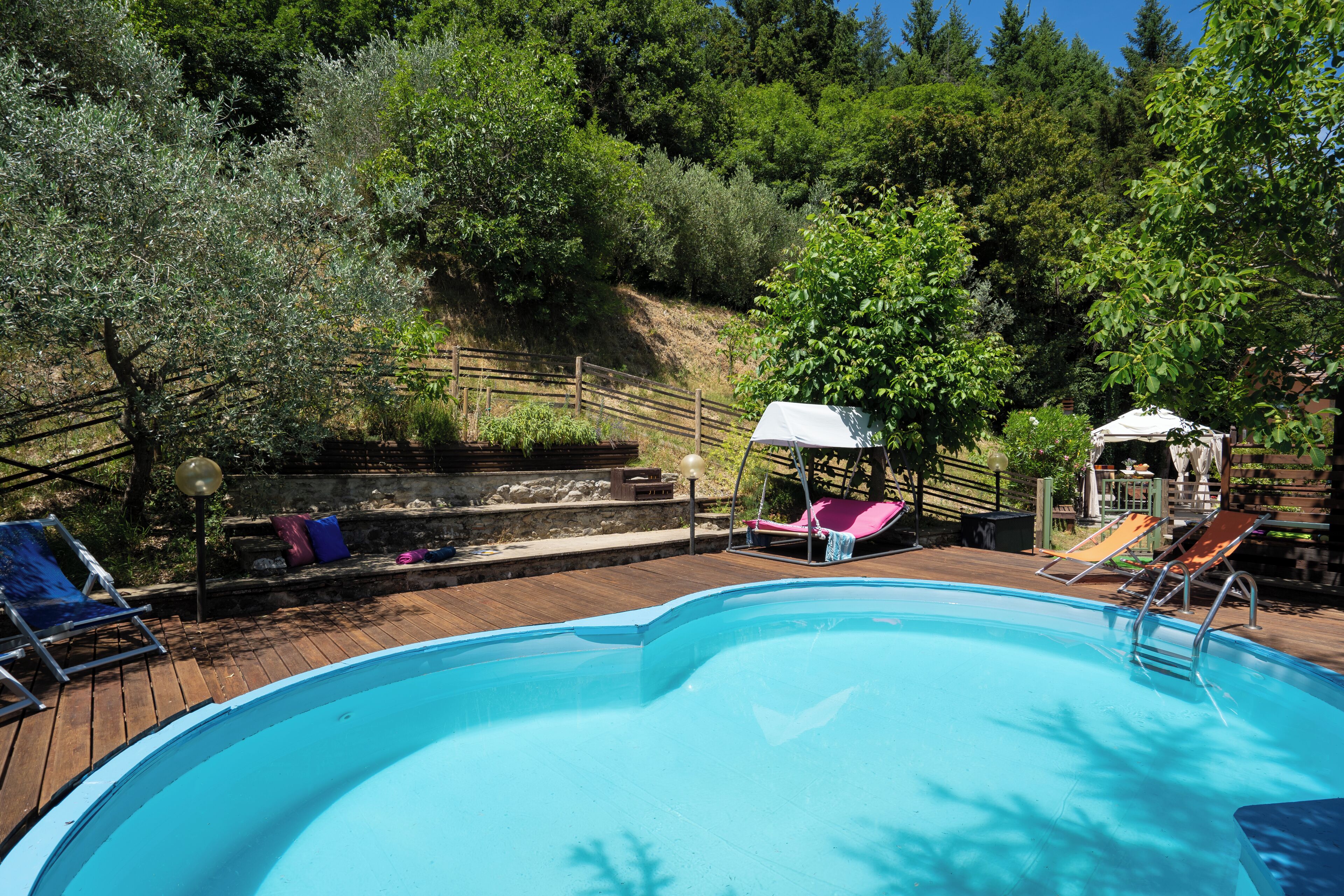 En swimmingpool med træterrasse, liggestole og en lille rutsjebane.