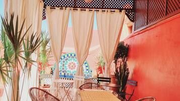 A covered patio area with wicker chairs, a table, and potted plants.