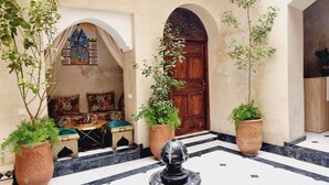 A courtyard with a fountain, potted plants, a sofa with cushions, and a wooden door. - Riad La Bigarade (Marrakech)