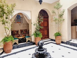 Un patio con una fuente, plantas en macetas, un sofá con cojines y una puerta de madera.
