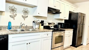 A modern kitchen with white cabinets, stainless steel appliances, a granite countertop, and decorative wall art. - Near Atrium & town, King/Queen/Pullout, NO stairs (Lincolnton)