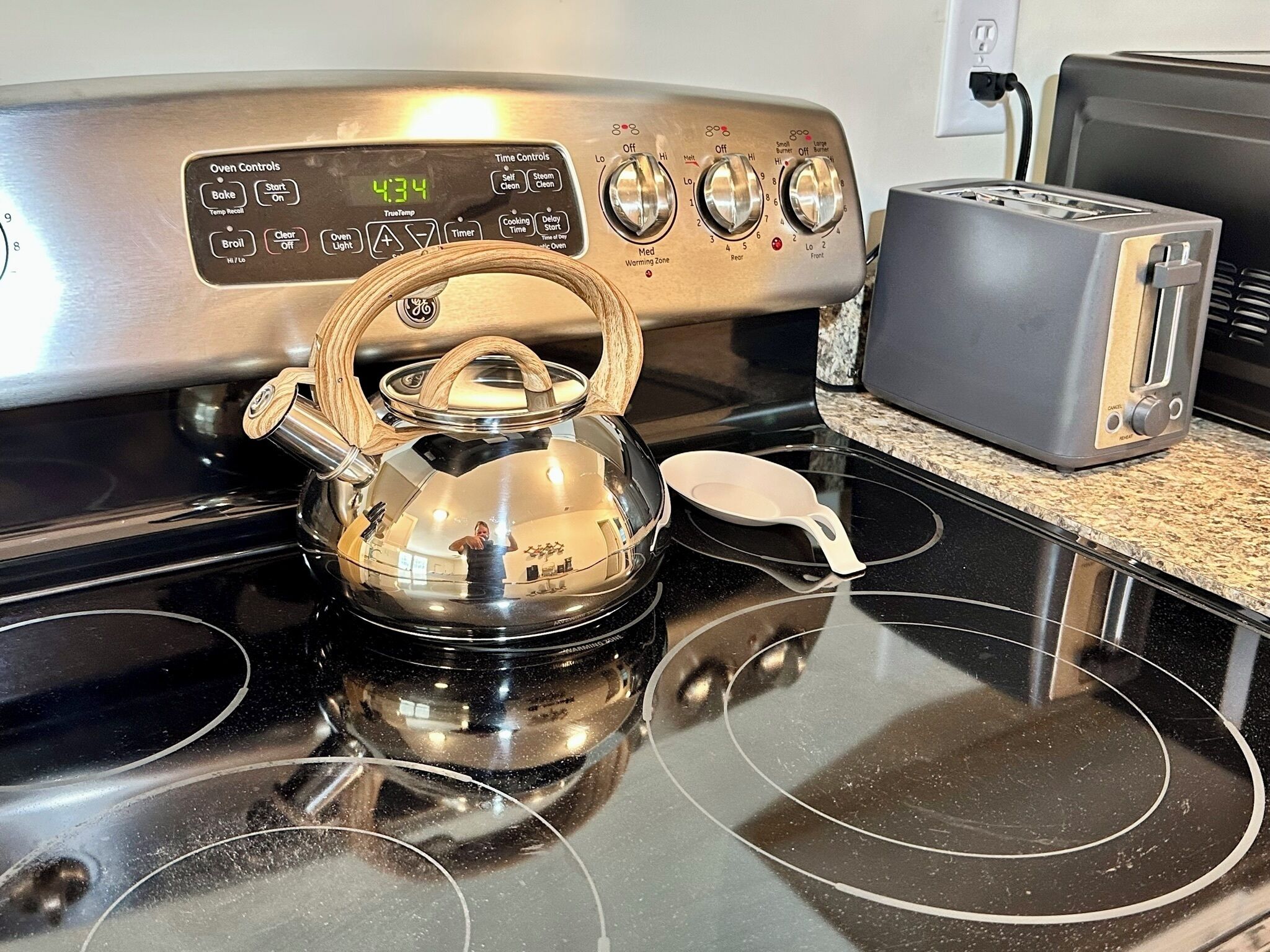 A kitchen with a stainless steel stove, a kettle, and a toaster on the counter.